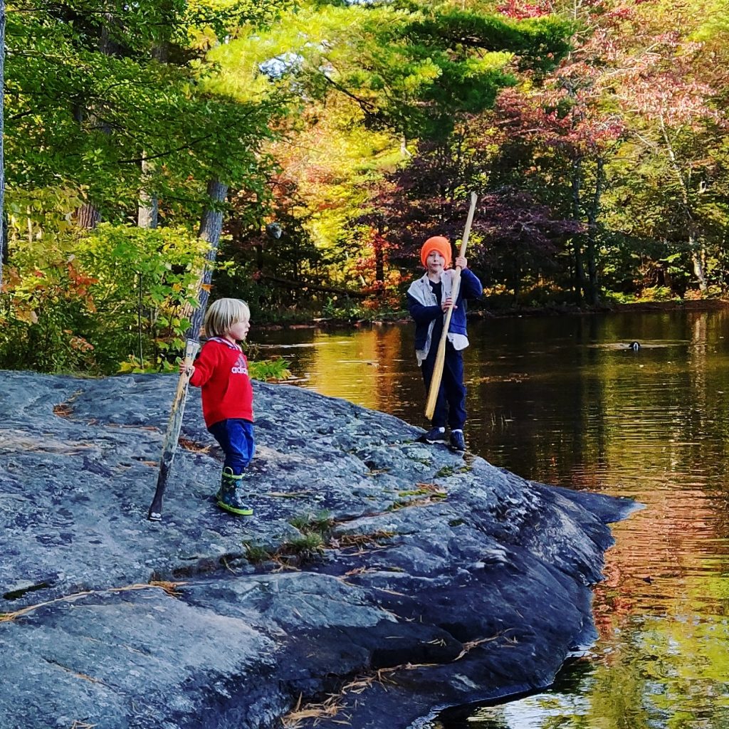 two boys on a rock by a lake reflecting fall foliage