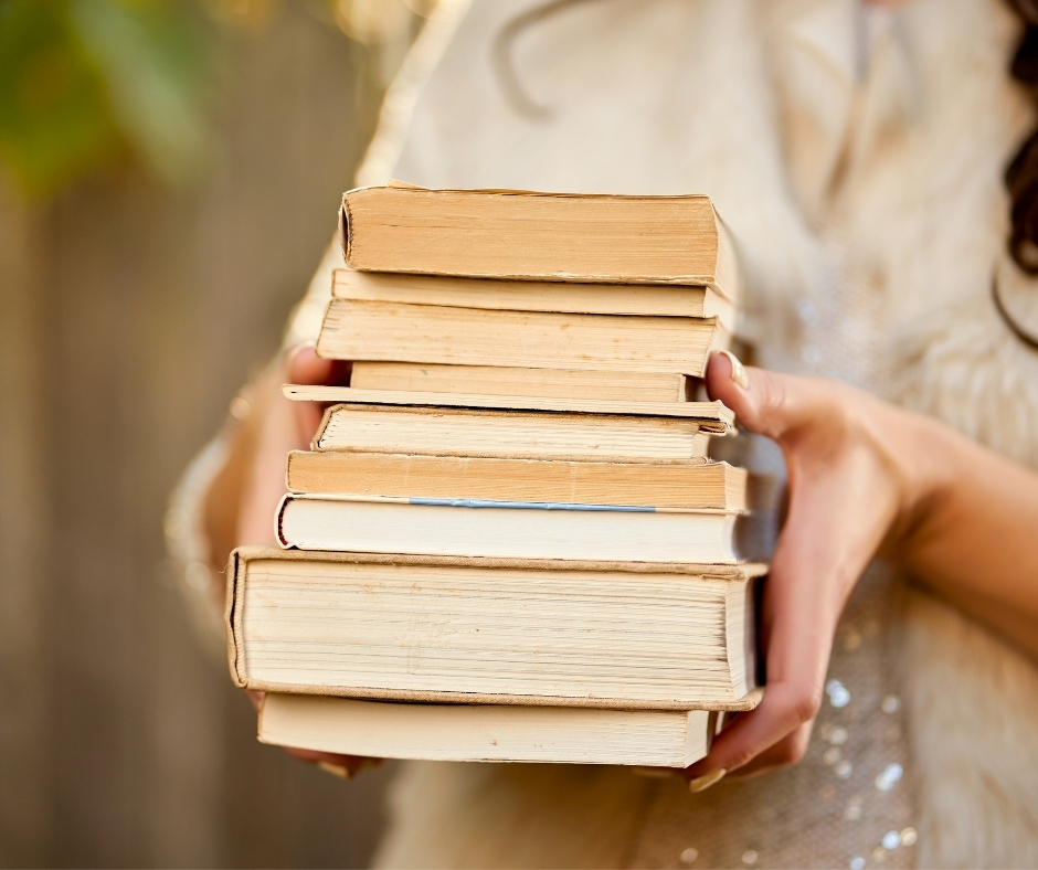 a stack of vintage books held in a woman's hands