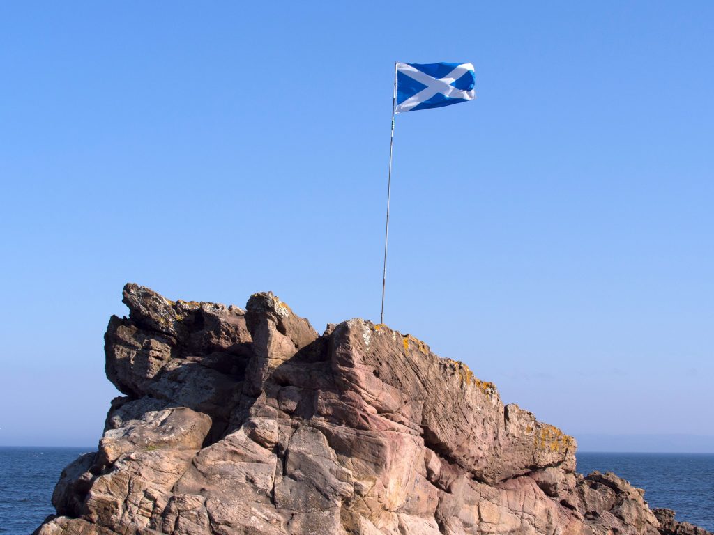 saltire flag, cross of st andrew on rocky outcropping by the ocean 