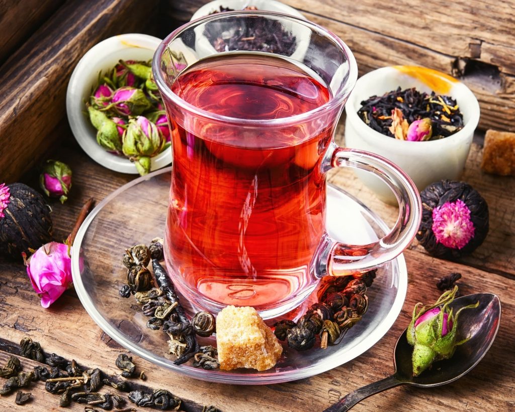 tall glass of pink tea with a handle centered on a wooden rustic table with rose hips and tea leaves surrounding