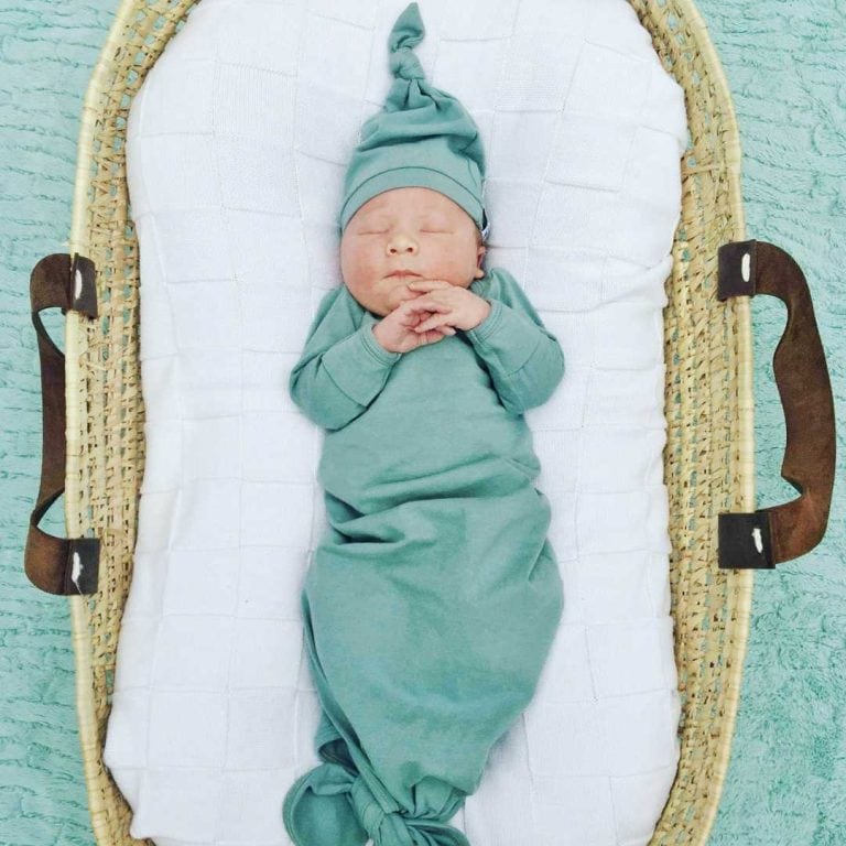 simple image of baby in moses basket with leather handles wearing a knotted organic gown in sage green