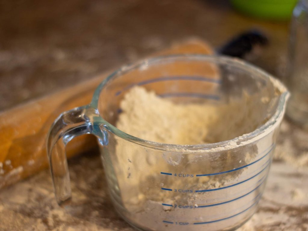 a large glass measuring cup of einkorn flour sits on a countertop with a rolling pin