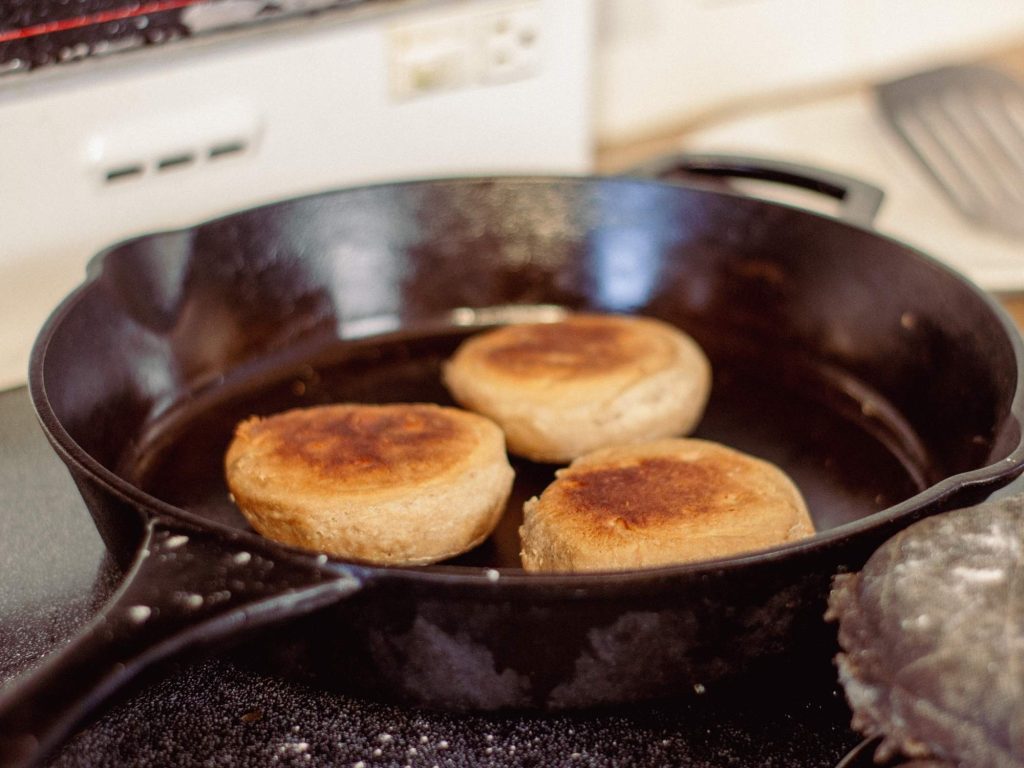 three english muffins cooking in a cast iron pan on a stovetop