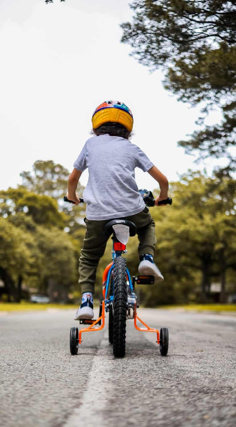 A young boy riding a bicycle with training wheels outdoors on a sunny day.